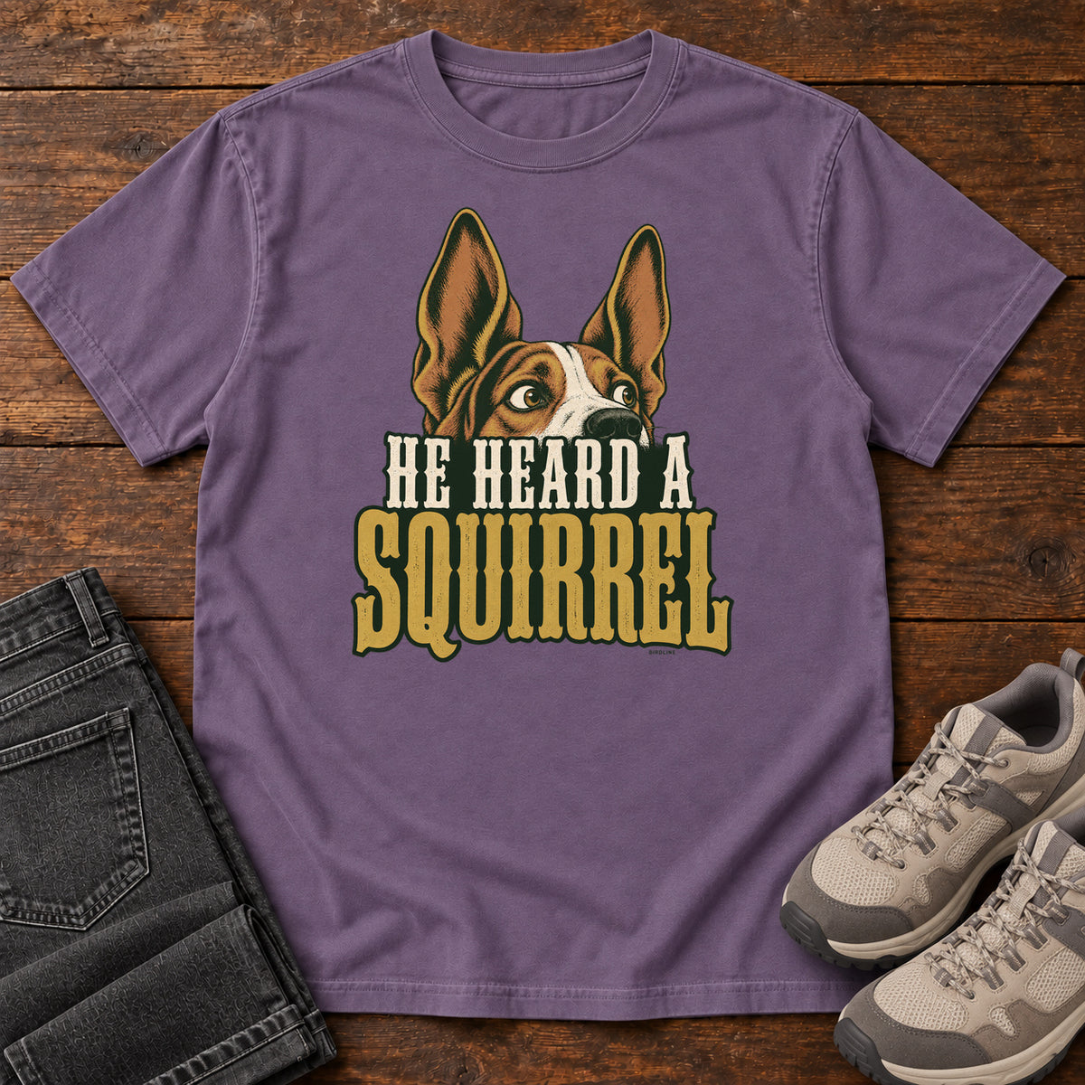 Grape He Heard a Squirrel T-Shirt with an alert dog with upright ears above He Heard a Squirrel lettering; front flat lay on wood.