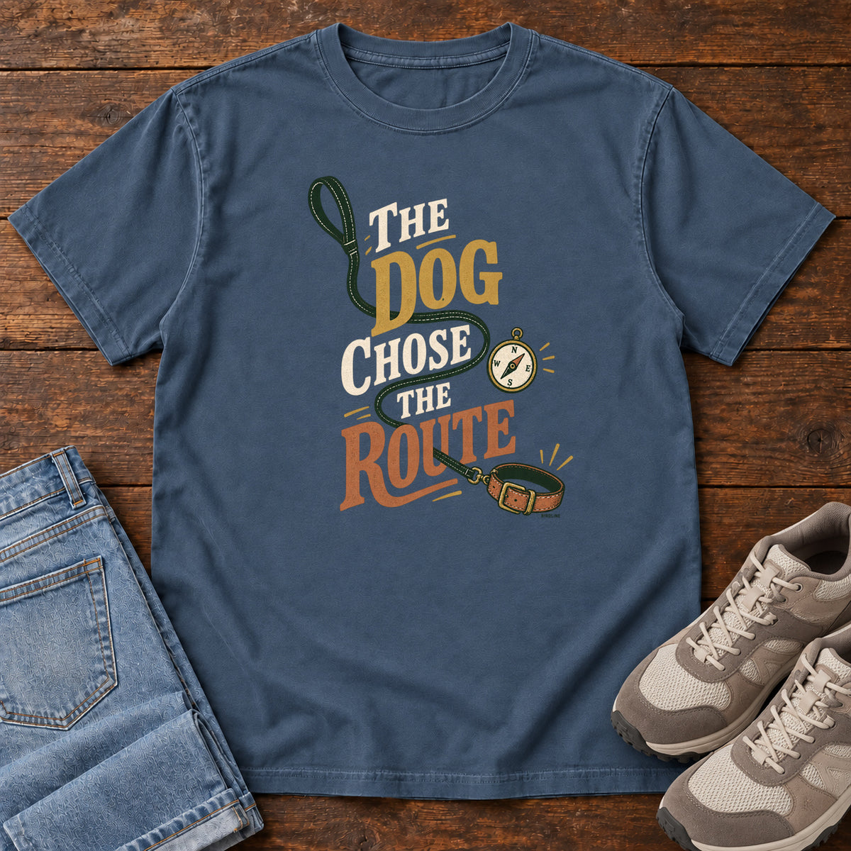 Midnight The Dog Chose the Route T-Shirt with a green leash, dog collar and compass around stacked lettering; front flat lay on wood.