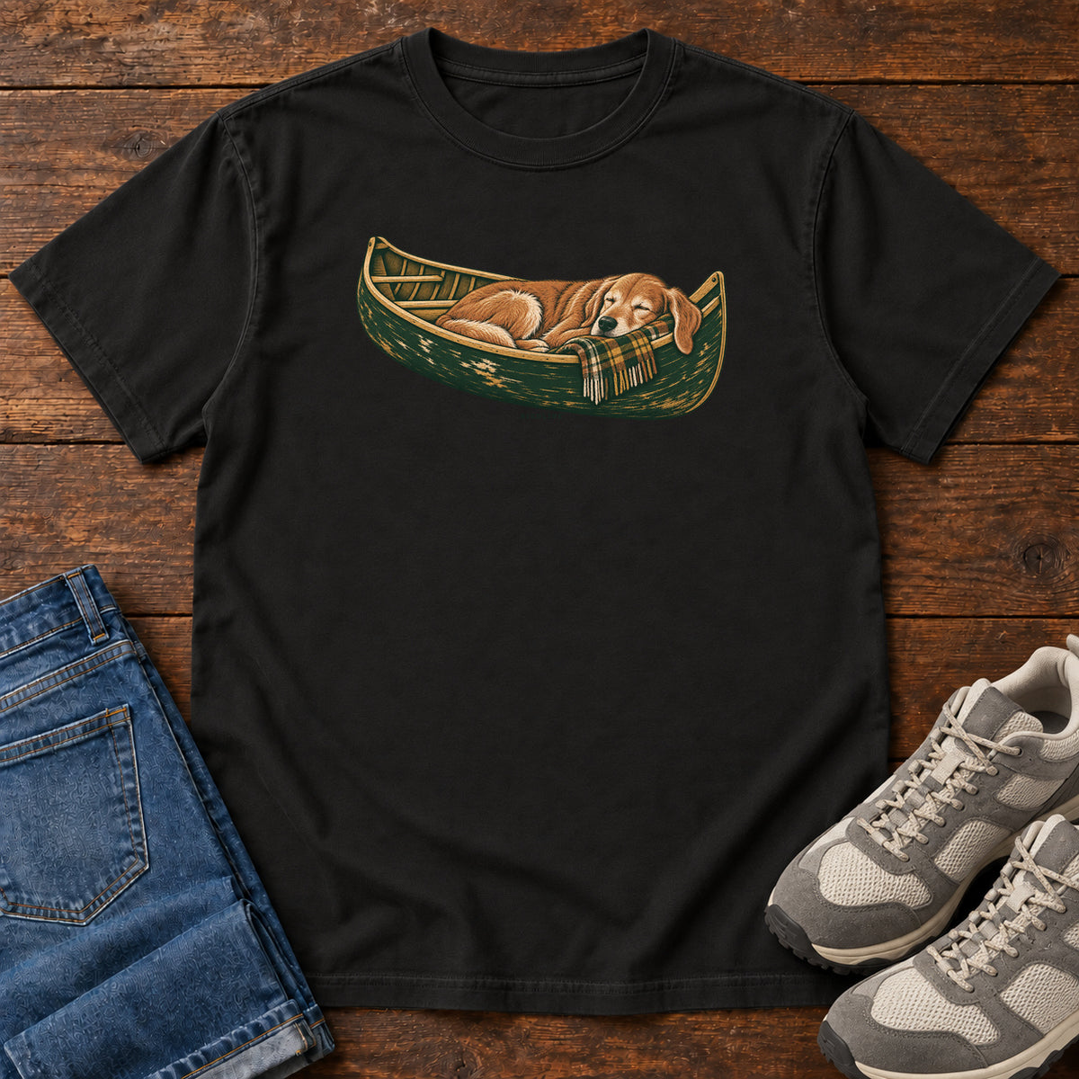 Black Retriever Canoe Birdline T-Shirt with a golden dog resting in a green canoe, front flat lay on wood.