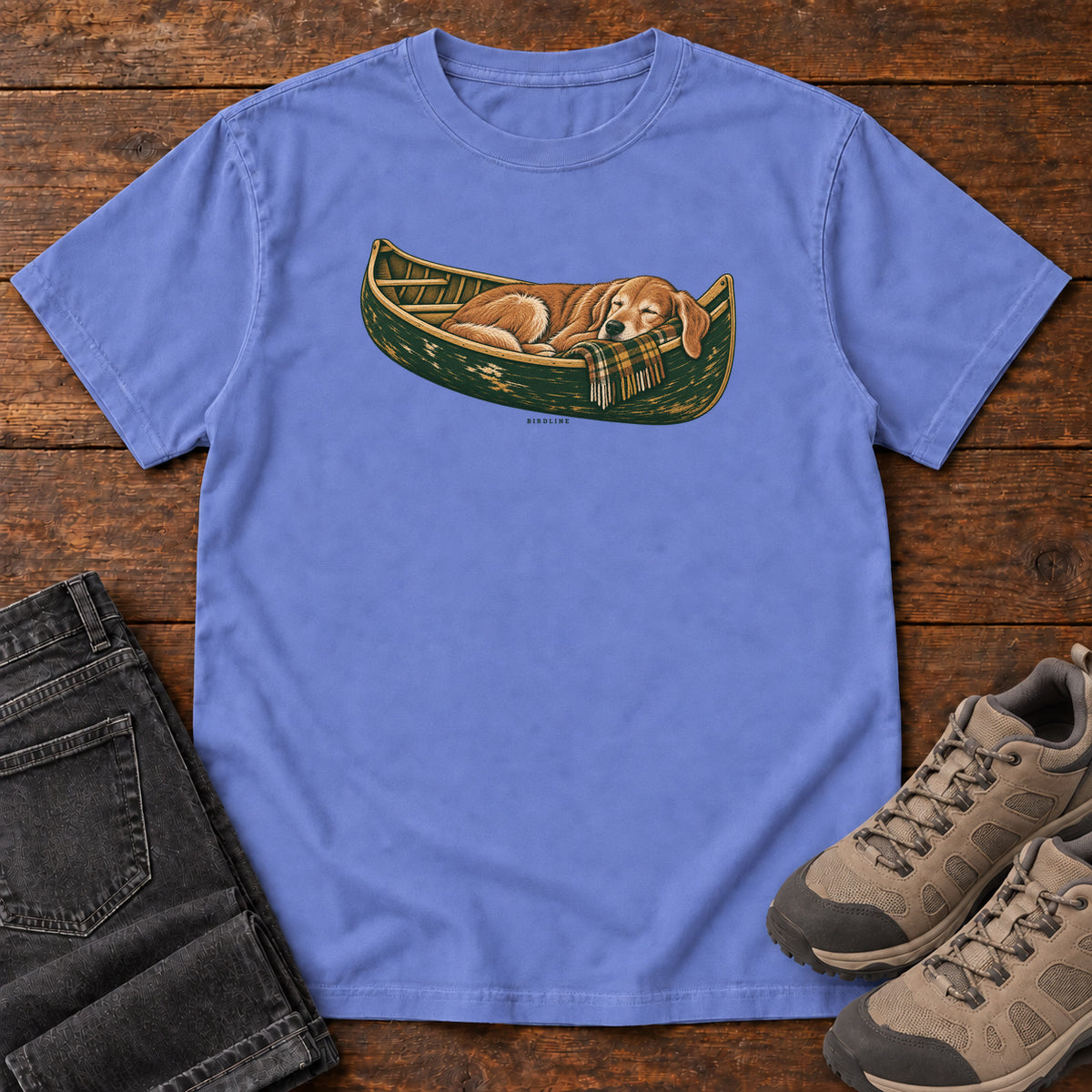 Flo Blue Retriever Canoe Birdline T-Shirt with a golden dog resting in a green canoe, front flat lay on wood.