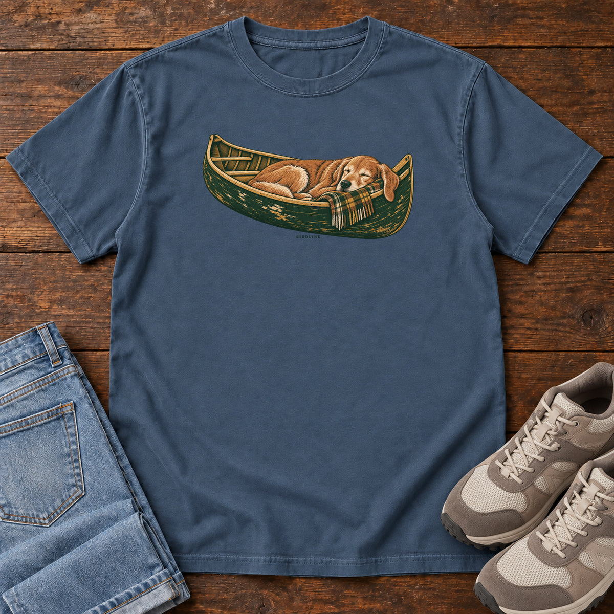 Midnight Retriever Canoe Birdline T-Shirt with a golden dog resting in a green canoe, front flat lay on wood.