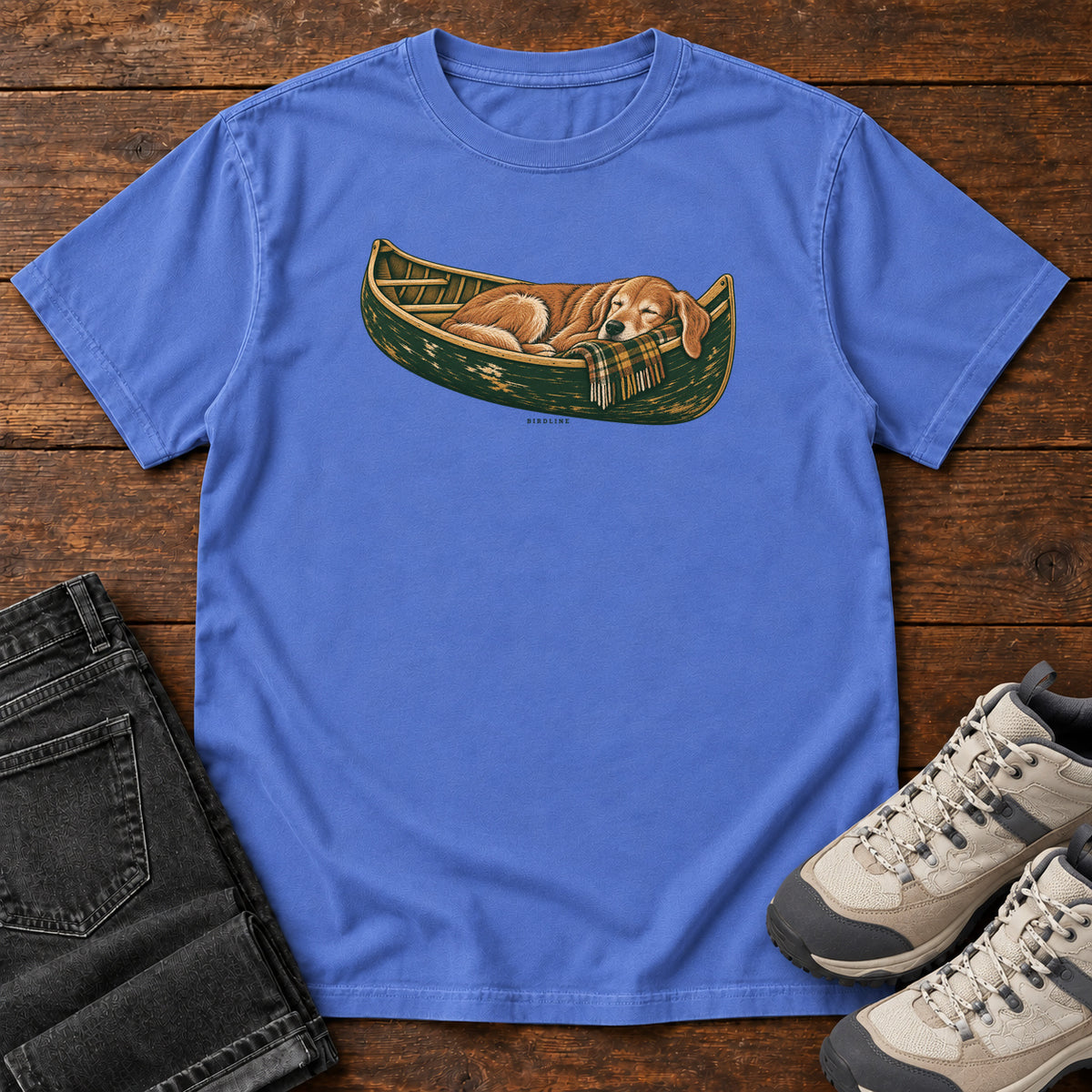 Mystic Blue Retriever Canoe Birdline T-Shirt with a golden dog resting in a green canoe, front flat lay on wood.