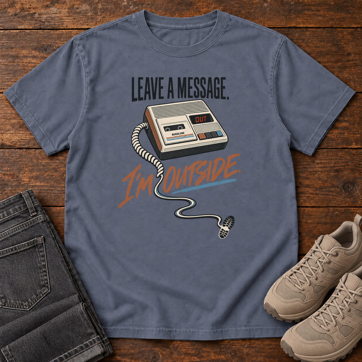 Denim Leave a Message I'm Outside T-Shirt with a retro answering machine, trailing cord and orange script, front flat lay on wood.