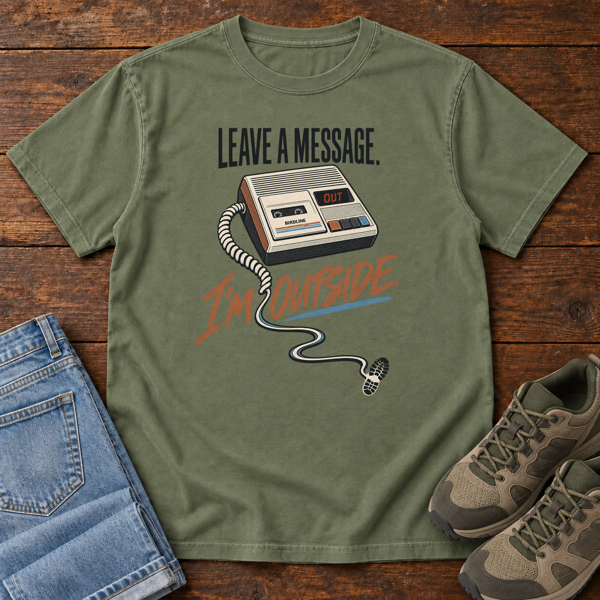 Moss Leave a Message I'm Outside T-Shirt with a retro answering machine, trailing cord and orange script, front flat lay on wood.