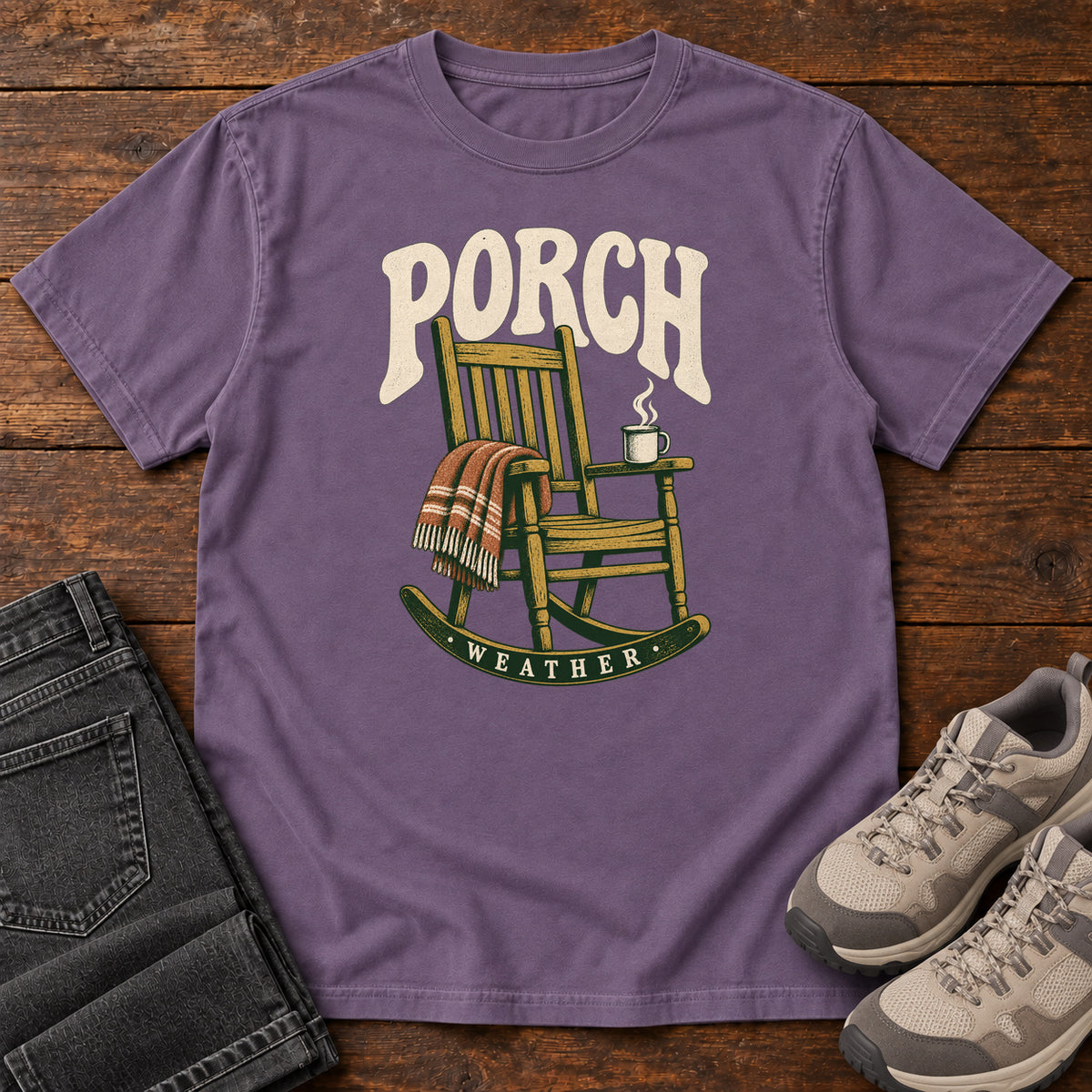 Grape Porch Weather T-Shirt with a wooden rocking chair with a striped blanket and steaming mug; front flat lay on wood.