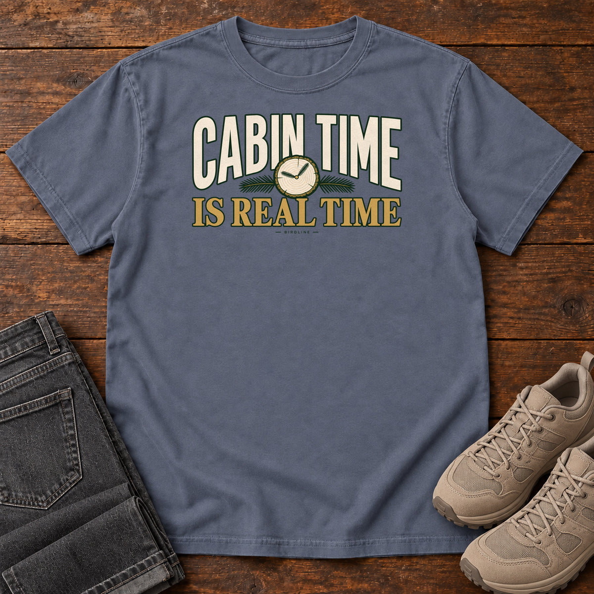 Denim Cabin Time Is Real Time T-Shirt with cream and gold lettering surrounding a small clock illustration, front flat lay on wood.