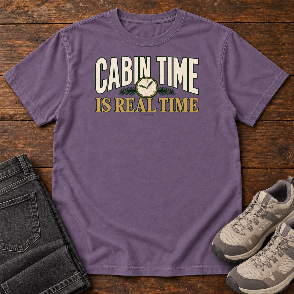 Grape Cabin Time Is Real Time T-Shirt with cream and gold lettering surrounding a small clock illustration, front flat lay on wood.