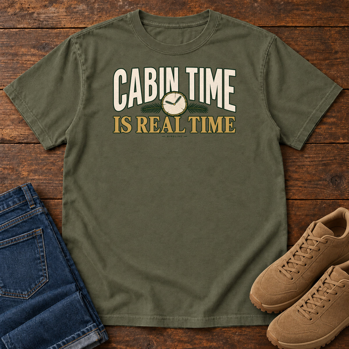 Sage Cabin Time Is Real Time T-Shirt with cream and gold lettering surrounding a small clock illustration, front flat lay on wood.