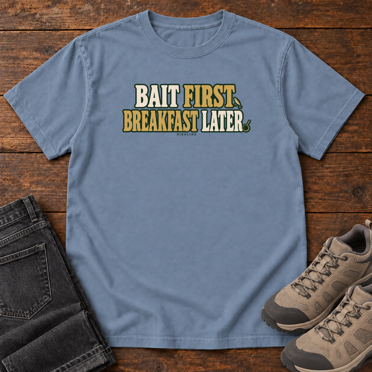 Blue Jean Bait First Breakfast Later T-Shirt with cream and gold Bait First Breakfast Later lettering; front flat lay on wood.