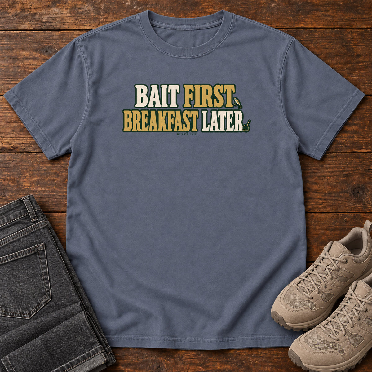 Denim Bait First Breakfast Later T-Shirt with cream and gold Bait First Breakfast Later lettering; front flat lay on wood.