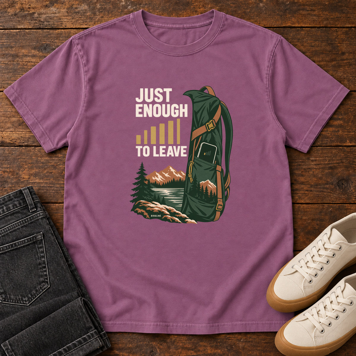 Berry Just Enough Signal to Leave T-Shirt with a green hiking backpack, mountains and gold signal bars beside cream lettering, front flat lay on wood.