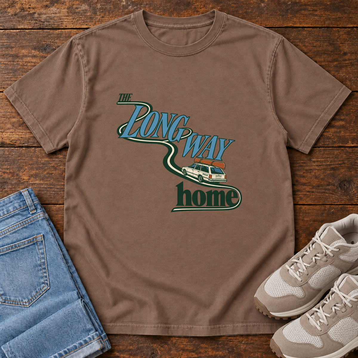 Espresso The Long Way Home T-Shirt with a station wagon on a winding road woven through The Long Way Home lettering; front flat lay on wood.