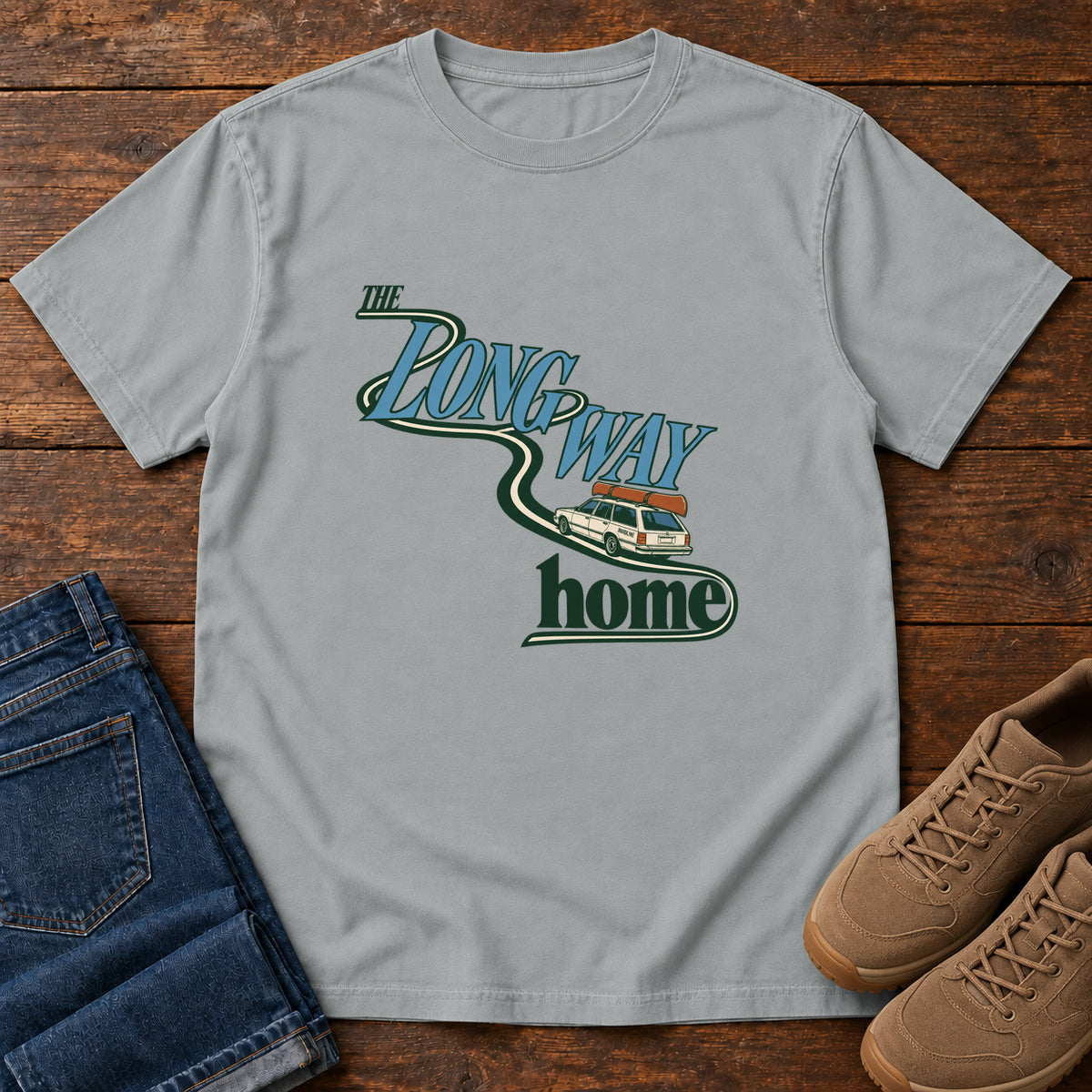 Granite The Long Way Home T-Shirt with a station wagon on a winding road woven through The Long Way Home lettering; front flat lay on wood.