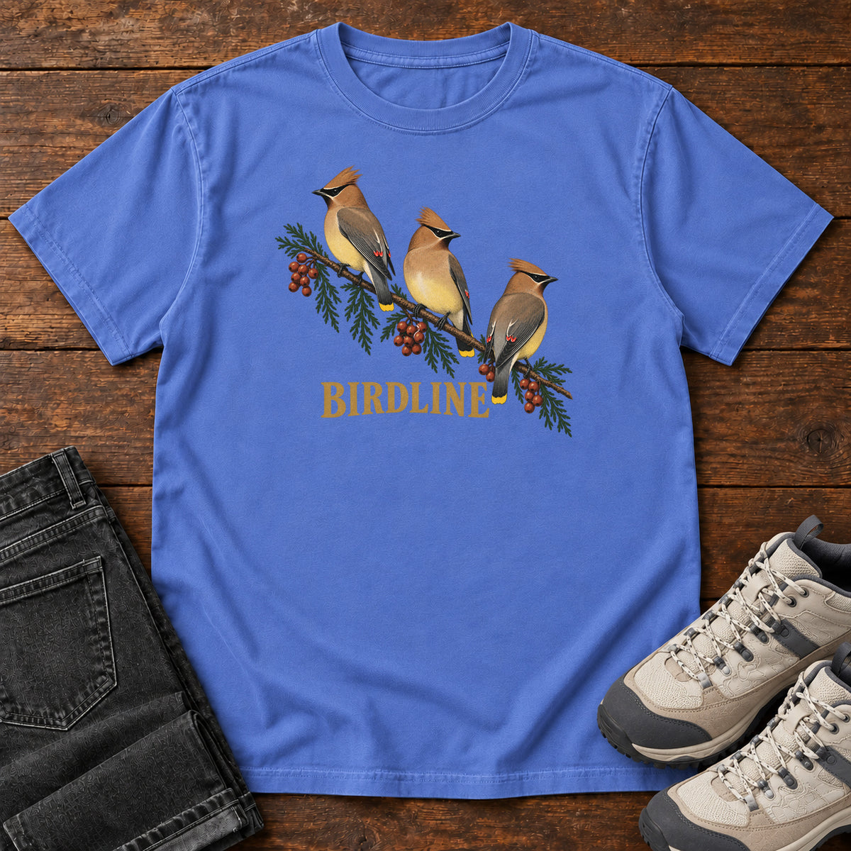 Mystic Blue Cedar Waxwings Birdline T-Shirt with three crested birds on a berry-laden evergreen branch; front flat lay on wood.