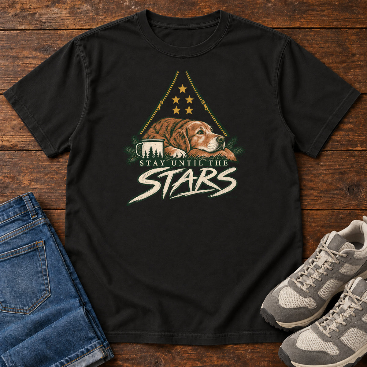 Black Stay Until the Stars T-Shirt with a resting brown dog beside a camp mug beneath gold stars and cream lettering, front flat lay on wood.