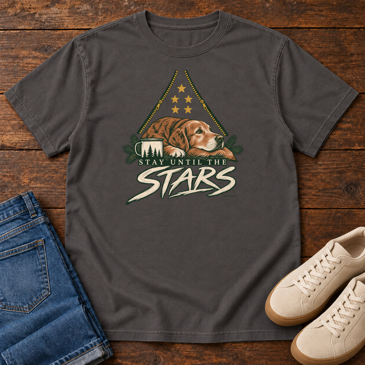 Graphite Stay Until the Stars T-Shirt with a resting brown dog beside a camp mug beneath gold stars and cream lettering, front flat lay on wood.