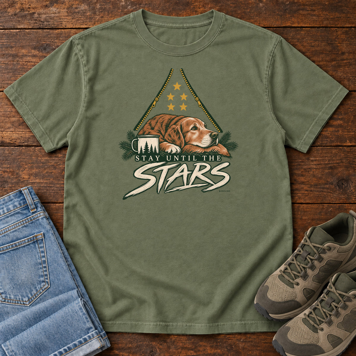 Moss Stay Until the Stars T-Shirt with a resting brown dog beside a camp mug beneath gold stars and cream lettering, front flat lay on wood.
