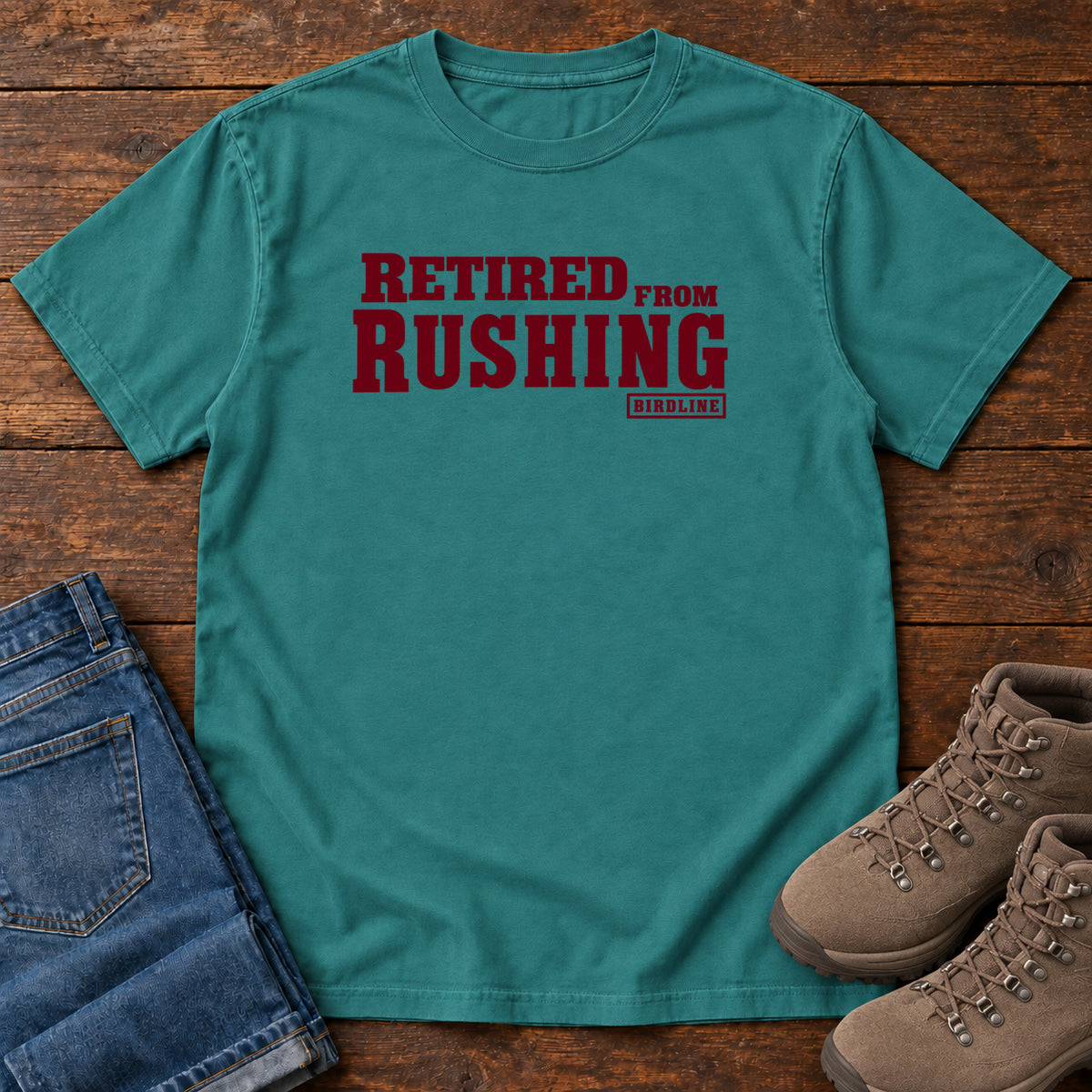 Emerald Retired From Rushing T-Shirt with burgundy Retired From Rushing lettering; front flat lay on wood.