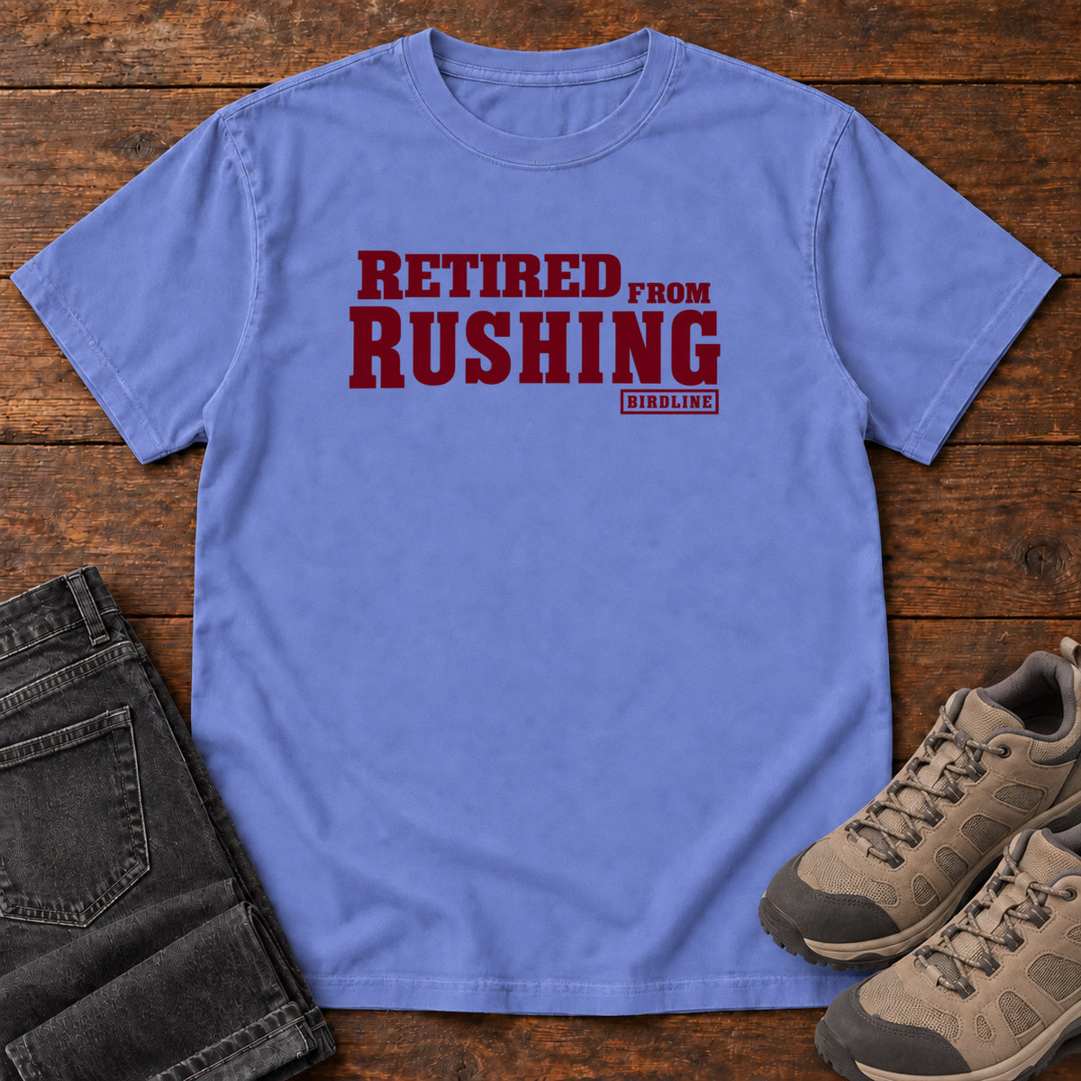 Flo Blue Retired From Rushing T-Shirt with burgundy Retired From Rushing lettering; front flat lay on wood.