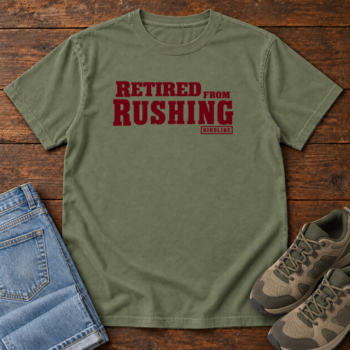 Moss Retired From Rushing T-Shirt with burgundy Retired From Rushing lettering; front flat lay on wood.