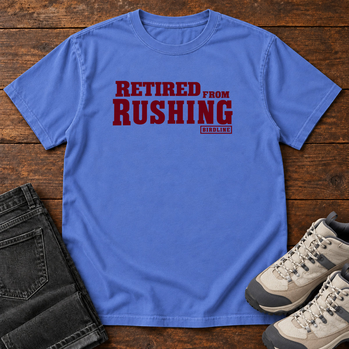 Mystic Blue Retired From Rushing T-Shirt with burgundy Retired From Rushing lettering; front flat lay on wood.