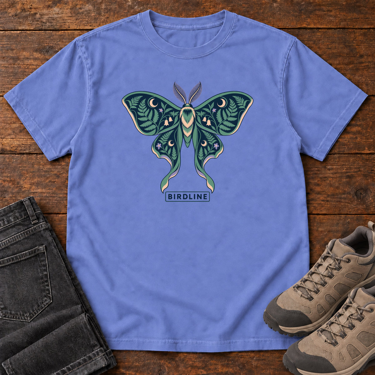 Botanical Moth T-Shirt in Flo Blue, front laid flat on wood, featuring a teal moth with patterned wings, leaves and crescent moons.