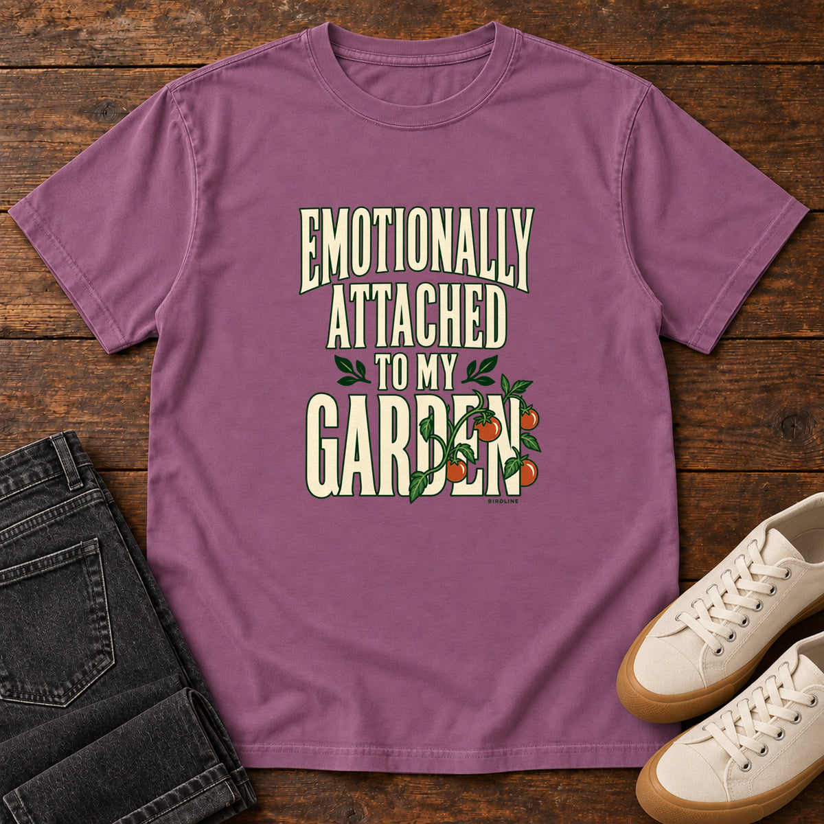 Berry Emotionally Attached to My Garden T-Shirt with cream lettering intertwined with a leafy vine and orange fruit, front flat lay on wood.