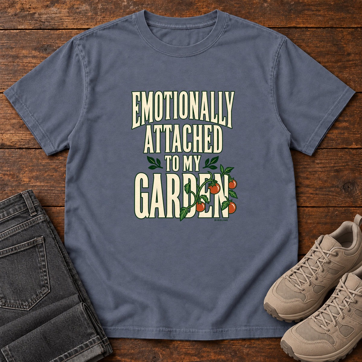 Denim Emotionally Attached to My Garden T-Shirt with cream lettering intertwined with a leafy vine and orange fruit, front flat lay on wood.