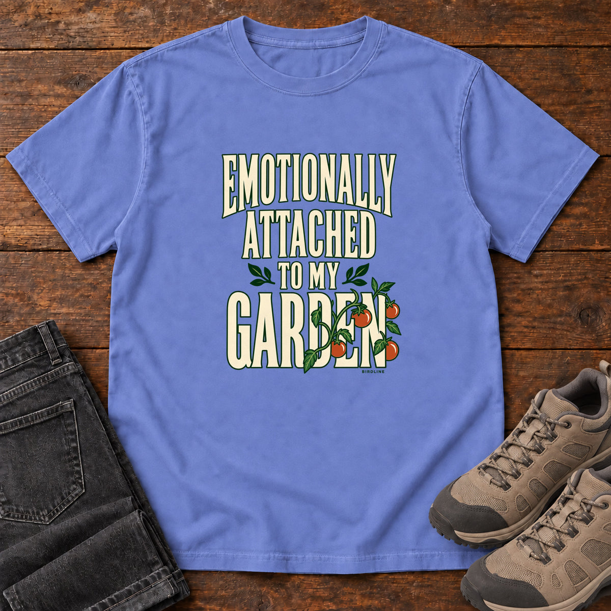 Flo Blue Emotionally Attached to My Garden T-Shirt with cream lettering intertwined with a leafy vine and orange fruit, front flat lay on wood.