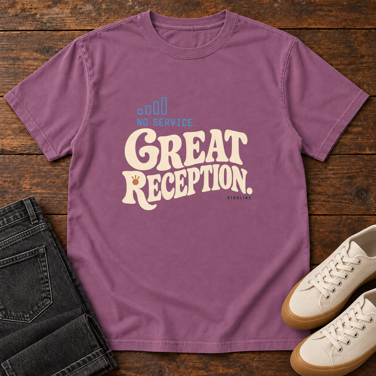 Berry No Service. Great Reception. T-Shirt with cream retro lettering and blue outlined phone-signal bars; front flat lay on wood.