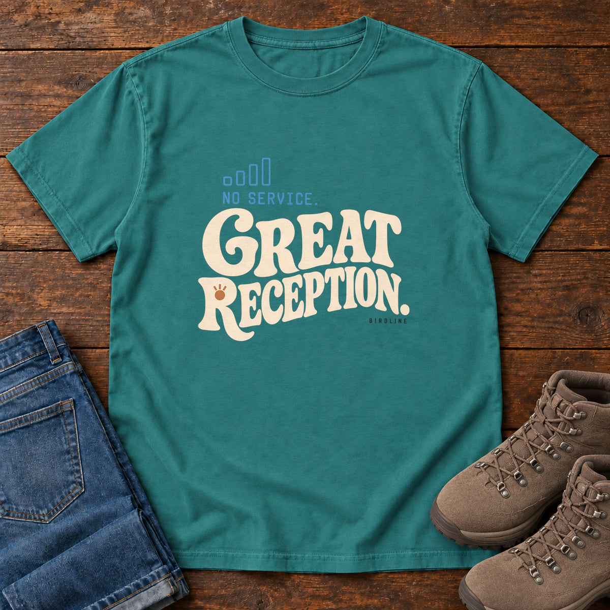 Emerald No Service. Great Reception. T-Shirt with cream retro lettering and blue outlined phone-signal bars; front flat lay on wood.
