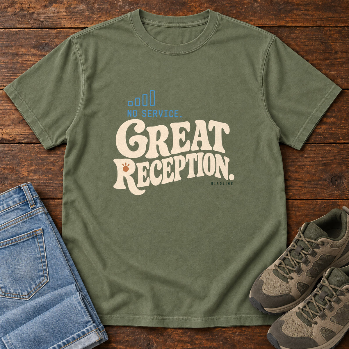 Moss No Service. Great Reception. T-Shirt with cream retro lettering and blue outlined phone-signal bars; front flat lay on wood.