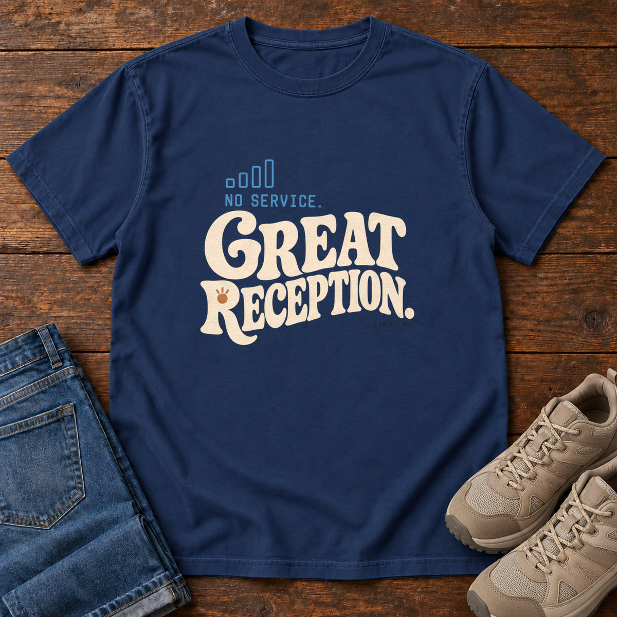 True Navy No Service. Great Reception. T-Shirt with cream retro lettering and blue outlined phone-signal bars; front flat lay on wood.