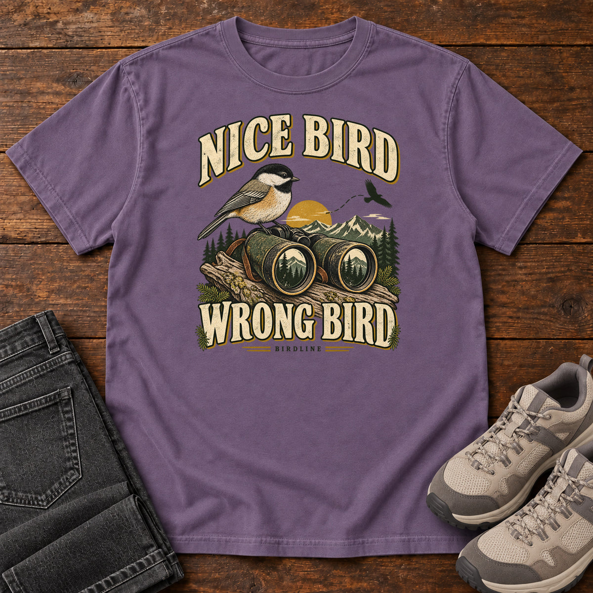 Grape Nice Bird. Wrong Bird. T-Shirt with a small black-capped bird on binoculars against mountains and a golden sun; front flat lay on wood.