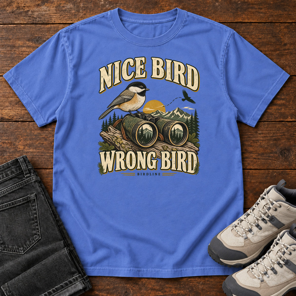 Mystic Blue Nice Bird. Wrong Bird. T-Shirt with a small black-capped bird on binoculars against mountains and a golden sun; front flat lay on wood.