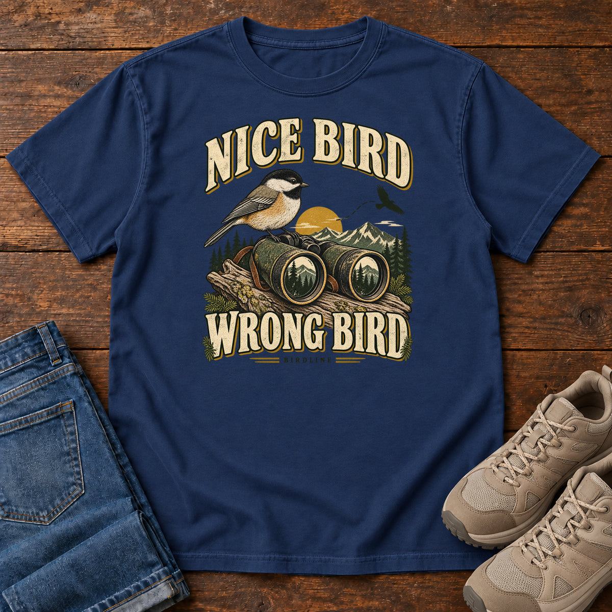 True Navy Nice Bird. Wrong Bird. T-Shirt with a small black-capped bird on binoculars against mountains and a golden sun; front flat lay on wood.