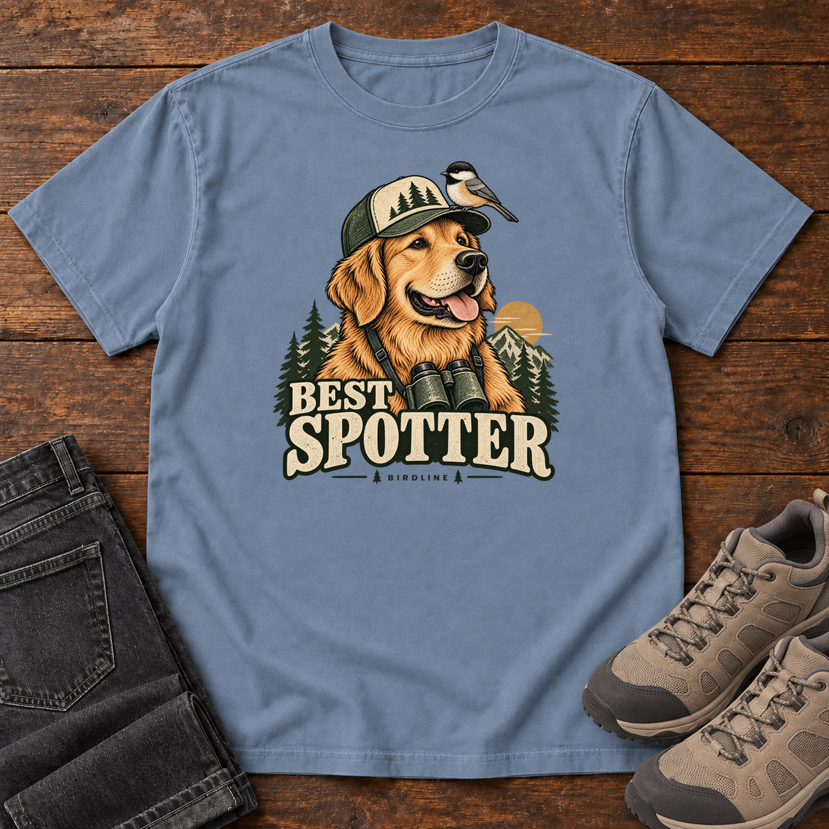 Blue Jean Best Spotter T-Shirt with a golden dog wearing a cap and binoculars, with a small bird perched on the cap, front flat lay on wood.