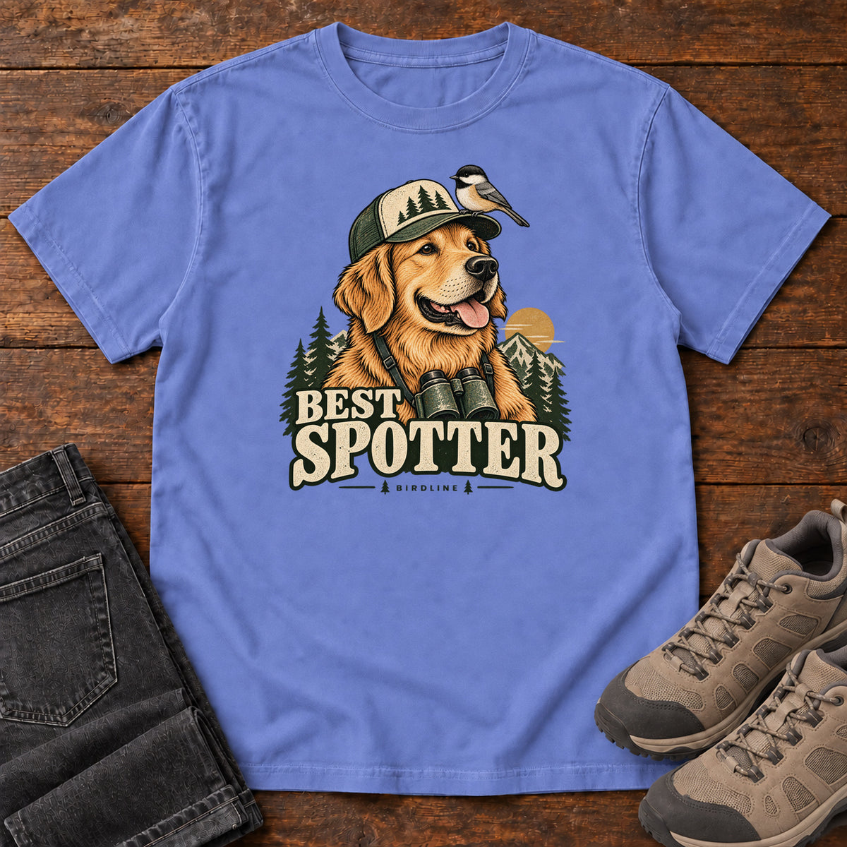 Flo Blue Best Spotter T-Shirt with a golden dog wearing a cap and binoculars, with a small bird perched on the cap, front flat lay on wood.