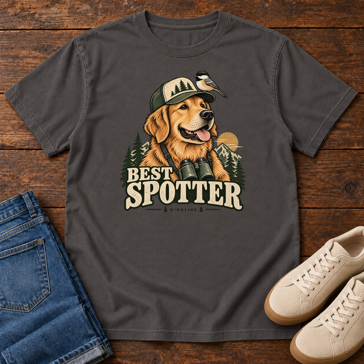 Graphite Best Spotter T-Shirt with a golden dog wearing a cap and binoculars, with a small bird perched on the cap, front flat lay on wood.