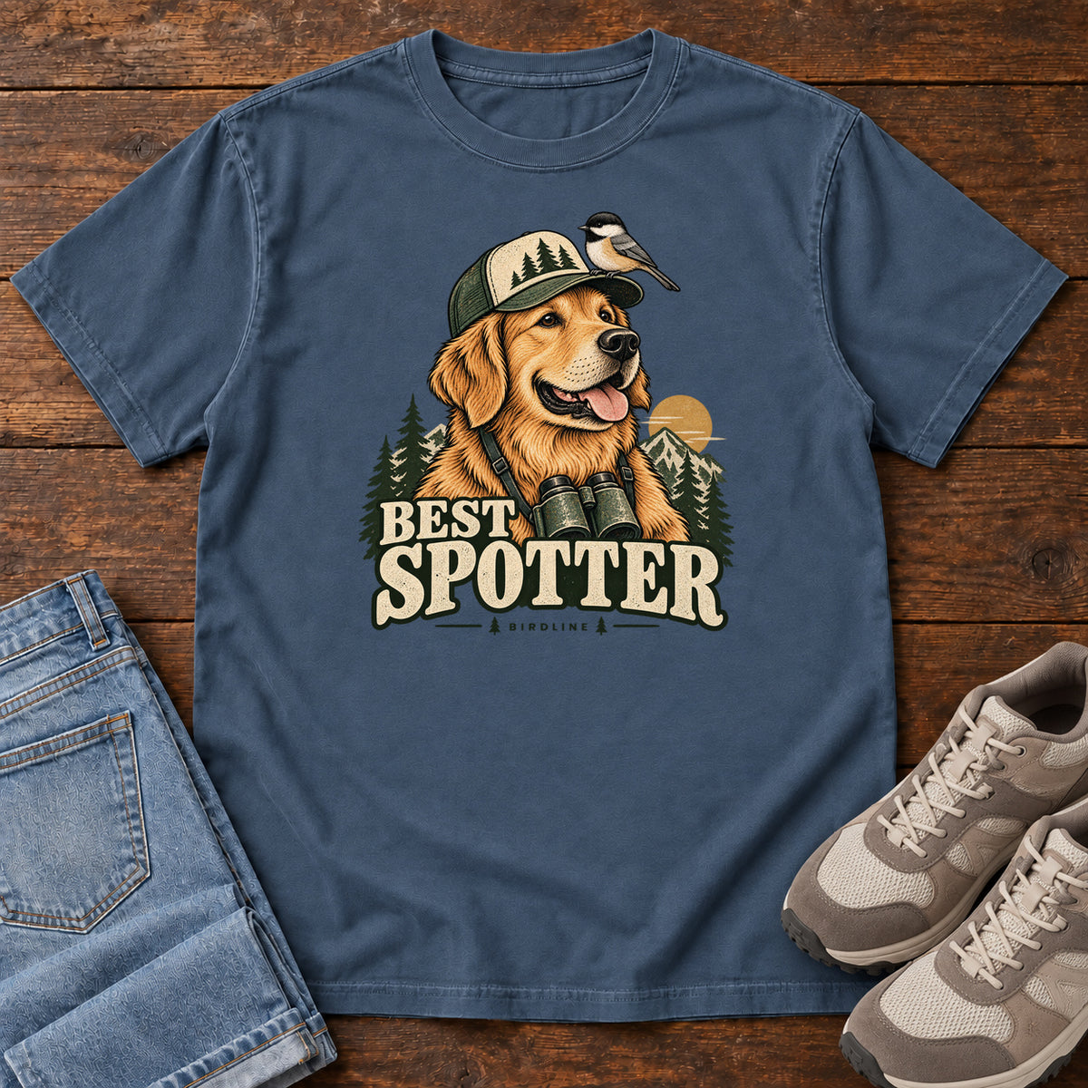 Midnight Best Spotter T-Shirt with a golden dog wearing a cap and binoculars, with a small bird perched on the cap, front flat lay on wood.