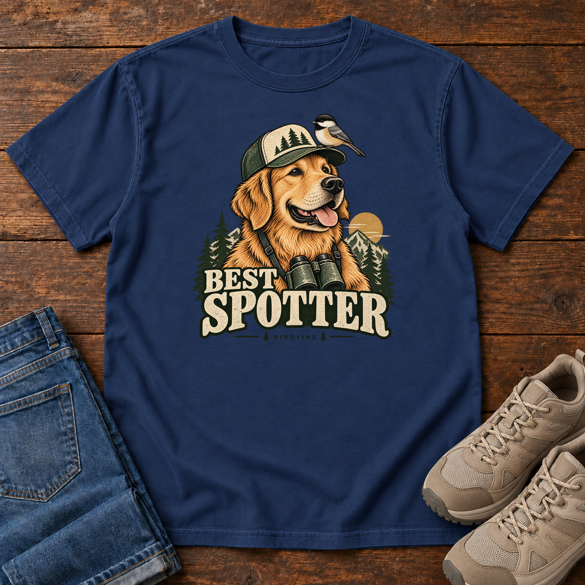 True Navy Best Spotter T-Shirt with a golden dog wearing a cap and binoculars, with a small bird perched on the cap, front flat lay on wood.