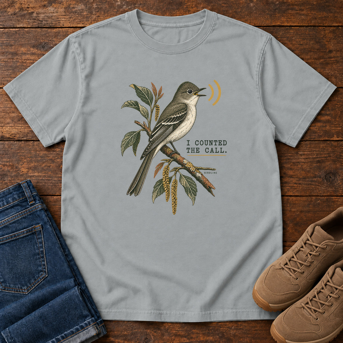 Granite I Counted the Call Songbird T-Shirt – Perched with a perched bird on a leafy branch and yellow sound-wave marks; front flat lay on wood.