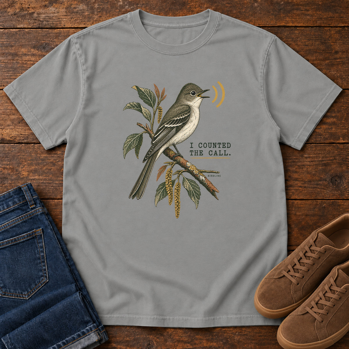 Grey I Counted the Call Songbird T-Shirt – Perched with a perched bird on a leafy branch and yellow sound-wave marks; front flat lay on wood.