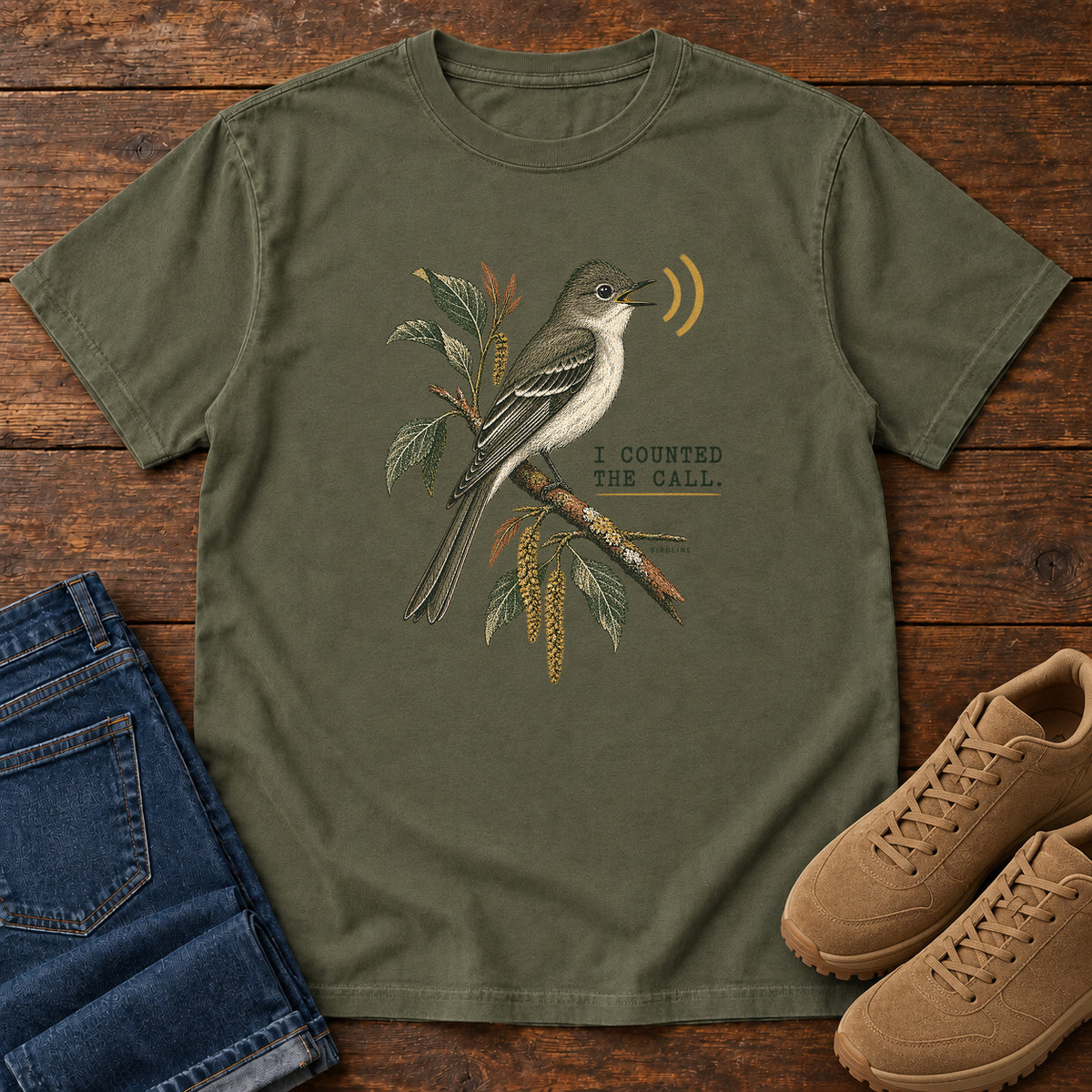 Sage I Counted the Call Songbird T-Shirt – Perched with a perched bird on a leafy branch and yellow sound-wave marks; front flat lay on wood.