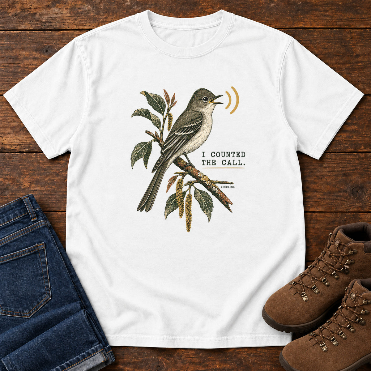 White I Counted the Call Songbird T-Shirt – Perched with a perched bird on a leafy branch and yellow sound-wave marks; front flat lay on wood.