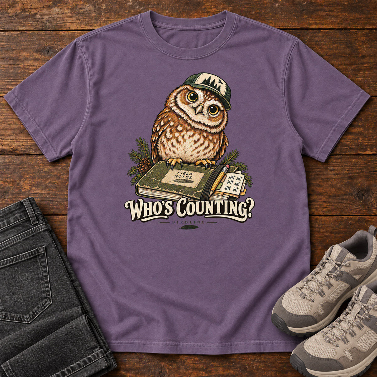 Grape Who's Counting? T-Shirt with a brown owl wearing a green cap beside a field notebook and checklist above cream lettering, front flat lay on wood.