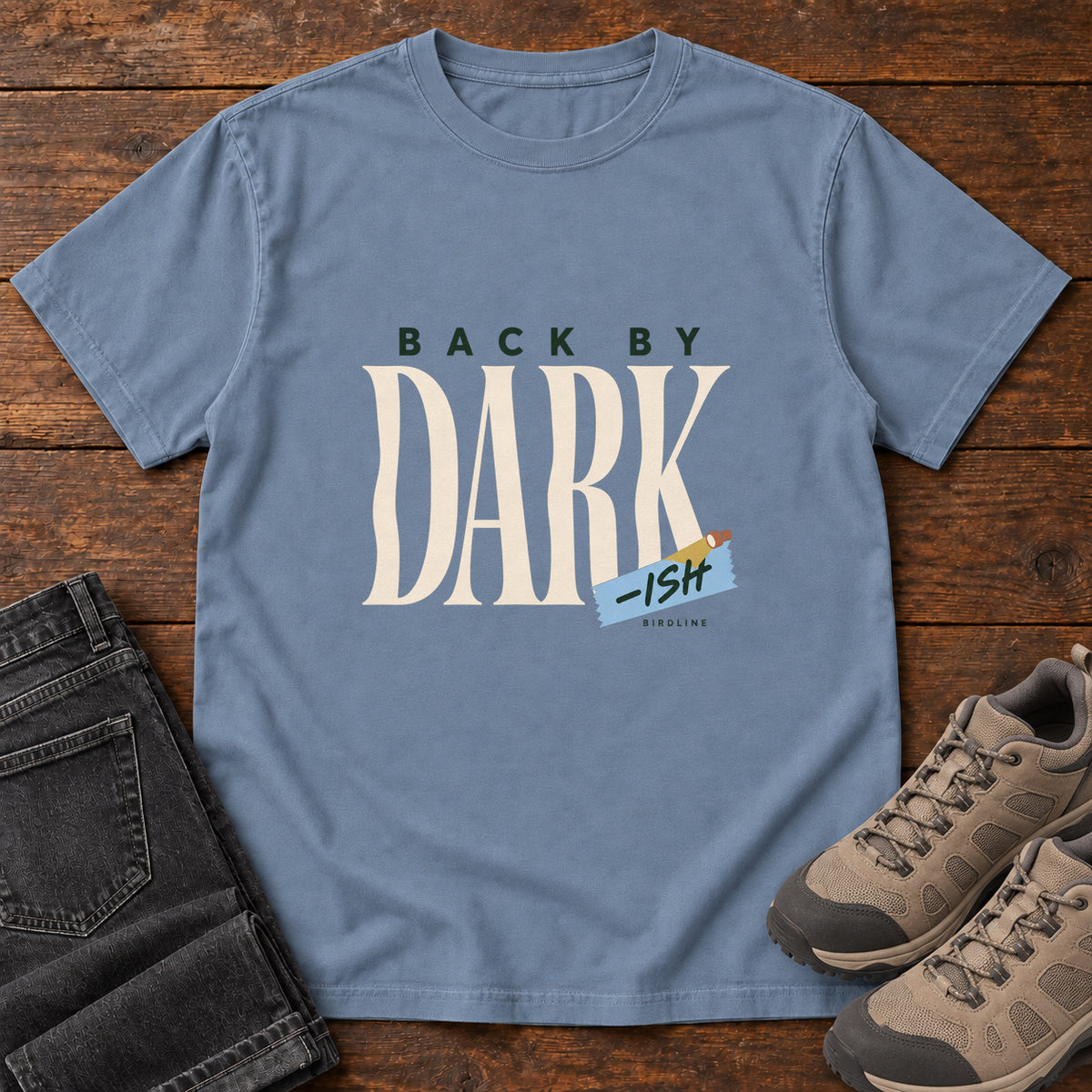 Blue Jean Back by Dark-ish T-Shirt with tall cream Dark lettering and a small blue -ish label, front flat lay on wood.