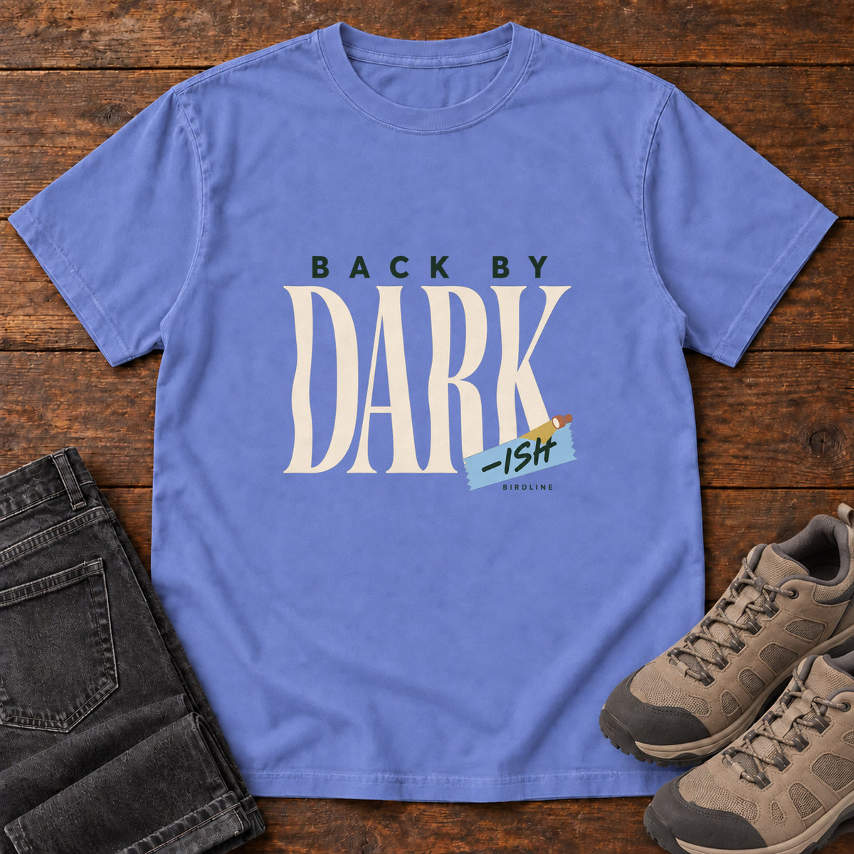 Flo Blue Back by Dark-ish T-Shirt with tall cream Dark lettering and a small blue -ish label, front flat lay on wood.
