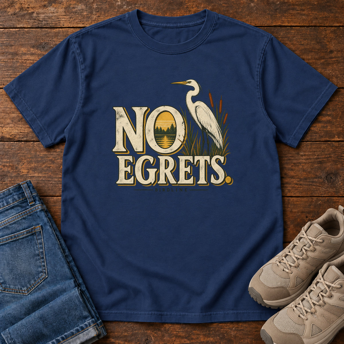 True Navy No Egrets. T-Shirt with a white long-necked wading bird beside reeds and lettering framing a sunset; front flat lay on wood.