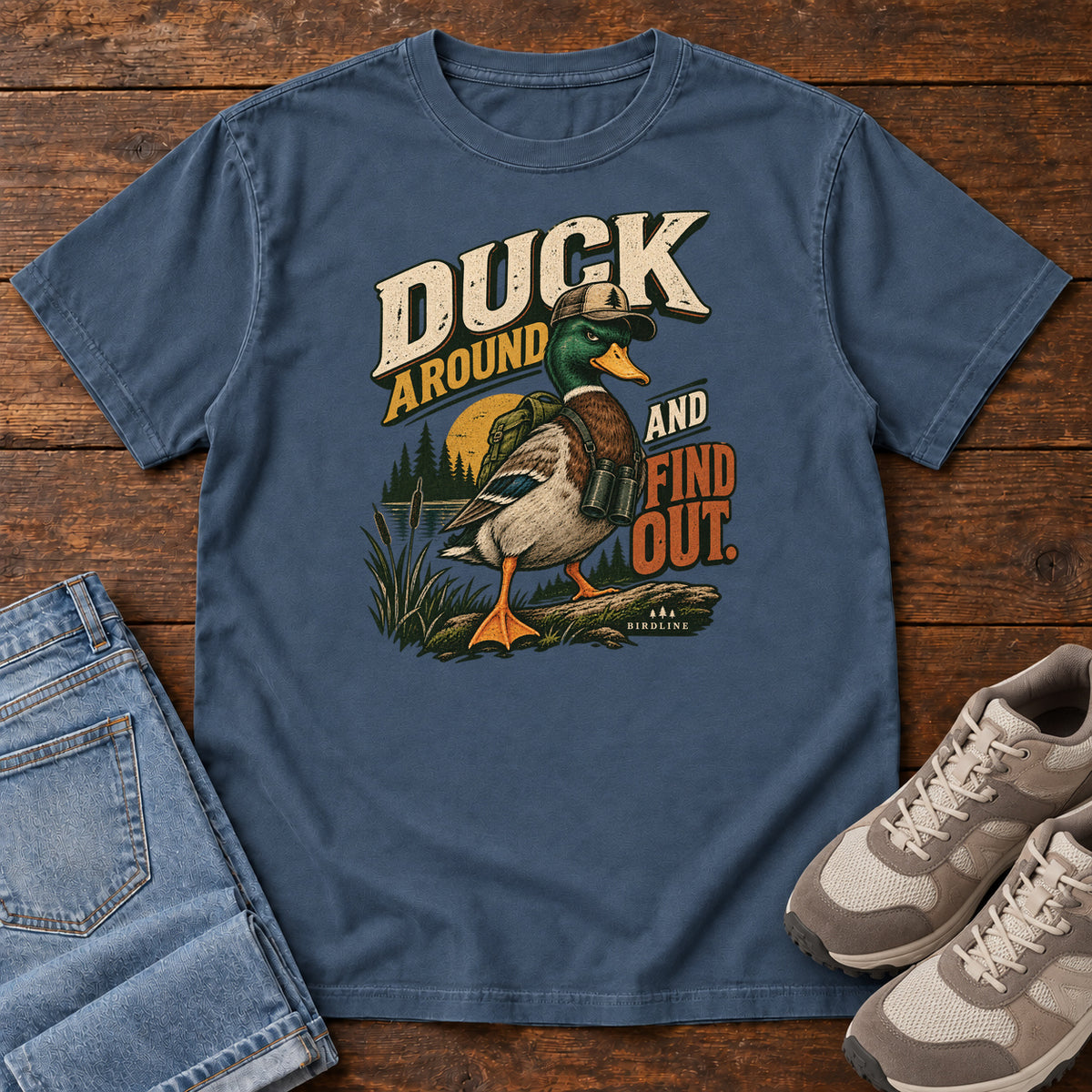 Midnight Duck Around and Find Out T-Shirt with a green-headed duck in a hat and vest beside marsh reeds and bold lettering, front flat lay on wood.
